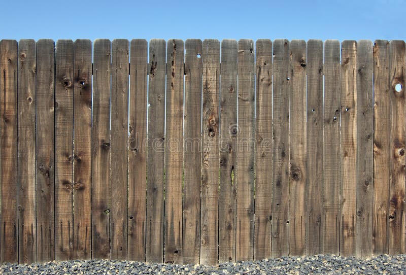 Wooden privacy fence with a gravel base and blue sky. Wooden privacy fence with a gravel base and blue sky