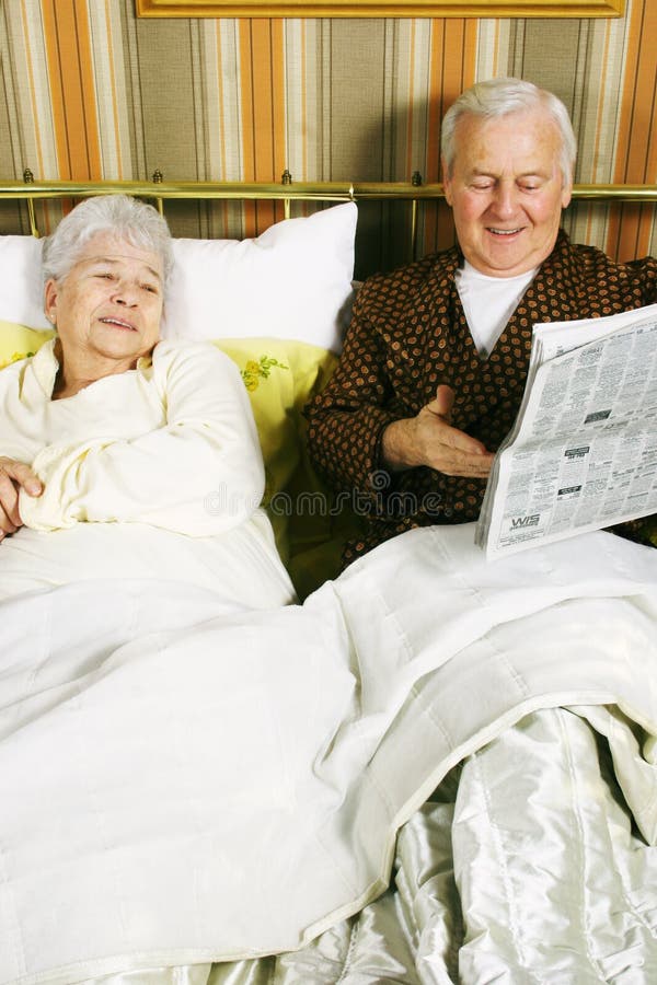 A retired couple discussing the latest news in their bed in the morning while reading a news paper. A retired couple discussing the latest news in their bed in the morning while reading a news paper.