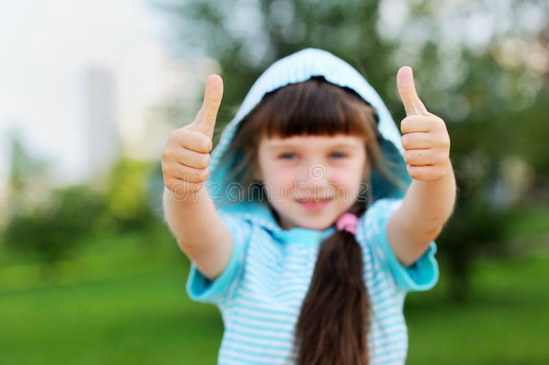 Retrato al aire libre de la muchacha linda del niño con los pulgares para arriba fotos de archivo libres de regalías Retrato al aire libre de la muchacha linda del niño con los pulgares para arriba fotos de archivo libres de regalías