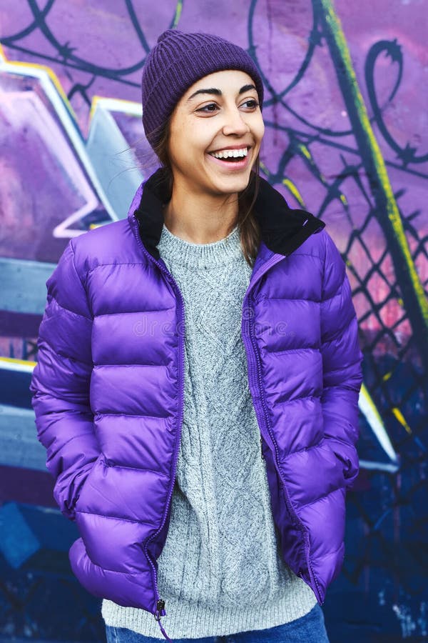 Retrato Al Aire Libre De Una Joven Atractiva Mujer Que Usa Una Chaqueta Violeta Y Sombrero De Punto Para Y Posar Contra Imagen de archivo - Imagen de azul, sonriente: