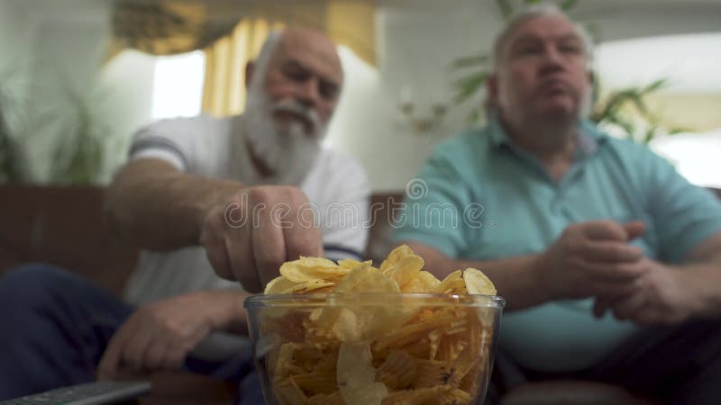 Retrato ascendente cercano de dos hombres mayores maduros que ven la TV en casa Amigos que miran fútbol del fútbol mientras que c almacen de video