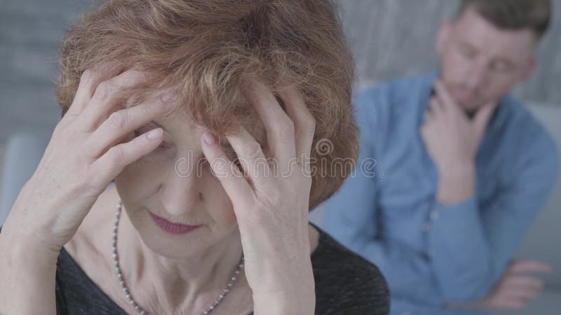 Retrato ascendente cercano de la mujer triste elegante madura mayor que lleva a cabo su cabeza en el primero plano Figura borrosa almacen de metraje de vídeo