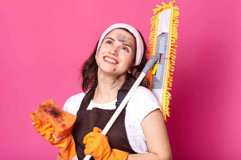 Retrato ascendente cercano del ama de casa feliz sonriente que mira para arriba, sosteniendo la escoba y la esponja en ambas mano imágenes de archivo libres de regalías Retrato ascendente cercano del ama de casa feliz sonriente que mira para arriba, sosteniendo la escoba y la esponja en ambas mano imágenes de archivo libres de regalías