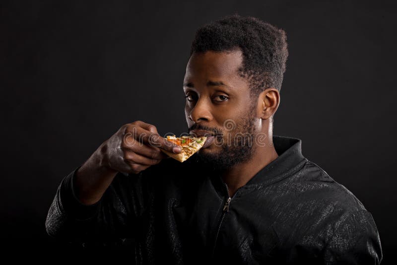 Retrato ascendente cercano del pedazo africano joven de la tenencia del hombre de pizza imágenes de archivo libres de regalías Retrato ascendente cercano del pedazo africano joven de la tenencia del hombre de pizza imágenes de archivo libres de regalías
