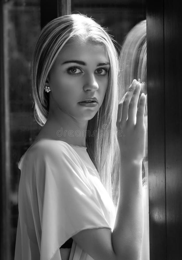 Retrato blanco y negro de la mujer que se inclina contra ventana imagenes de archivo Retrato blanco y negro de la mujer que se inclina contra ventana imagenes de archivo