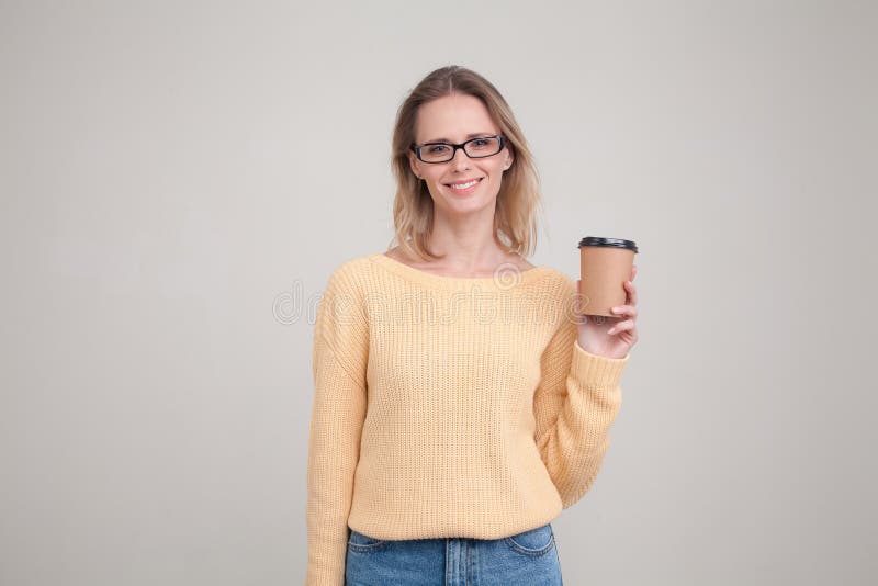 Retrato da cintura-acima da mulher loura que guarda o tamp?o do caf? em suas m?os e que sorri, olhando a c?mera camiseta amarela fotografia de stock royalty free Retrato da cintura-acima da mulher loura que guarda o tamp?o do caf? em suas m?os e que sorri, olhando a c?mera camiseta amarela fotografia de stock royalty free