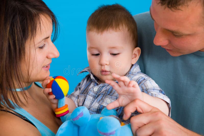 Portrait of happy casual family. Baby boy ( 1 year old ) and young parents father and mother together against blue background, smiling. Portrait of happy casual family. Baby boy ( 1 year old ) and young parents father and mother together against blue background, smiling.