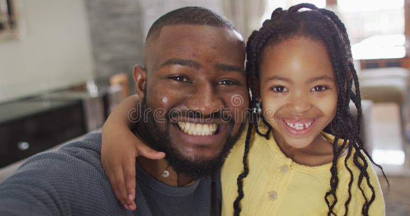 Retrato da feliz filha e pai da américa africana tomando selfie no sofá