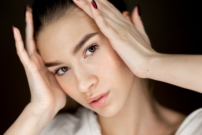 Retrato da menina bonita nova dos marrom-olhos com a composição natural que guarda suas mãos em sua cabeça foto de stock Retrato da menina bonita nova dos marrom-olhos com a composição natural que guarda suas mãos em sua cabeça foto de stock