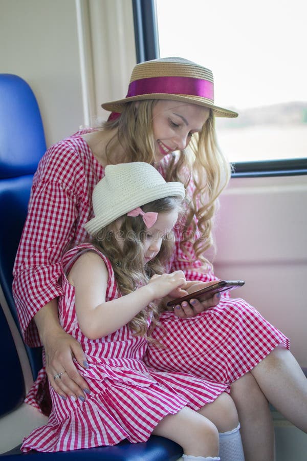 Retrato da menina caucasiano com sua mamã nos chapéus com cabelo ondulado usando um smartphone no trem fotografia de stock Retrato da menina caucasiano com sua mamã nos chapéus com cabelo ondulado usando um smartphone no trem fotografia de stock