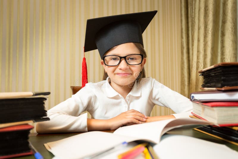 Retrato da menina de sorriso no chapéu da graduação que senta-se na aba foto de stock Retrato da menina de sorriso no chapéu da graduação que senta-se na aba foto de stock