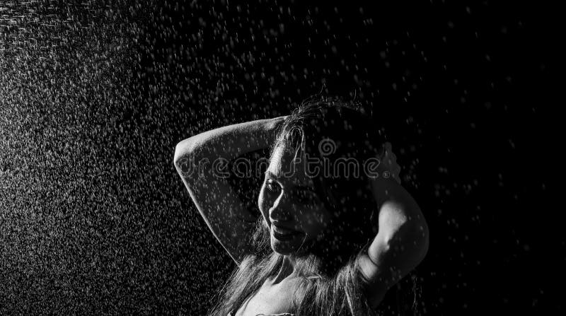 Retrato da menina e água felizes do espirro em sua cara modelo fêmea bonito no fundo preto foto de stock Retrato da menina e água felizes do espirro em sua cara modelo fêmea bonito no fundo preto foto de stock