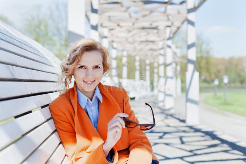 Retrato da mulher de negócio ou do estudante de sorriso feliz da forma com os óculos de sol que sentam-se no banco no parque, con fotos de stock royalty free Retrato da mulher de negócio ou do estudante de sorriso feliz da forma com os óculos de sol que sentam-se no banco no parque, con fotos de stock royalty free