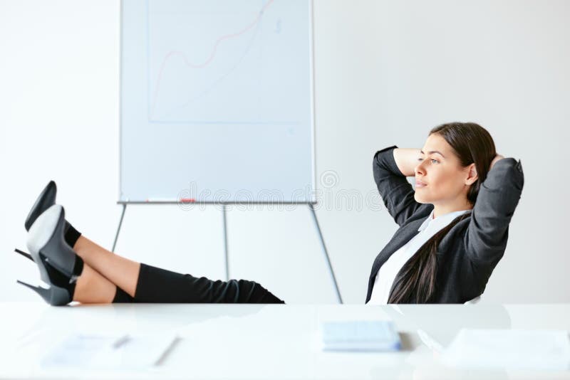Retrato da mulher de negócio relaxado que senta-se com pés na mesa