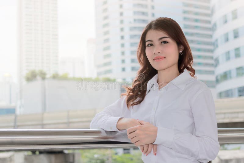 Retrato da mulher de negócios asiática nova atrativa que olha na câmera na construção urbana com fundo do efeito da luz do sol Li imagem de stock Retrato da mulher de negócios asiática nova atrativa que olha na câmera na construção urbana com fundo do efeito da luz do sol Li imagem de stock