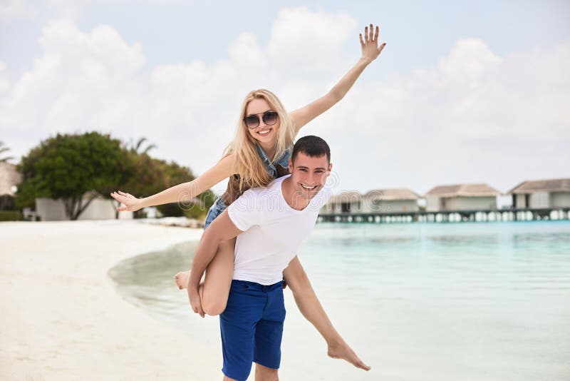 Retrato da mulher levando de sorriso do homem no seu para trás ao longo da costa de mar Indivíduo que dá às cavalitas o passeio à fotografia de stock royalty free Retrato da mulher levando de sorriso do homem no seu para trás ao longo da costa de mar Indivíduo que dá às cavalitas o passeio à fotografia de stock royalty free