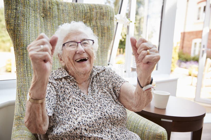 Retrato da mulher superior entusiasmado que senta-se na cadeira na sala de estar do lar de idosos