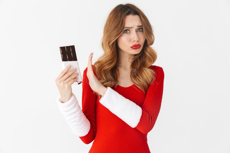 Retrato da mulher séria 20s que veste o traje vermelho de Santa Claus que guarda e que rejeita a barra de chocolate, isolado sobr fotografia de stock Retrato da mulher séria 20s que veste o traje vermelho de Santa Claus que guarda e que rejeita a barra de chocolate, isolado sobr fotografia de stock
