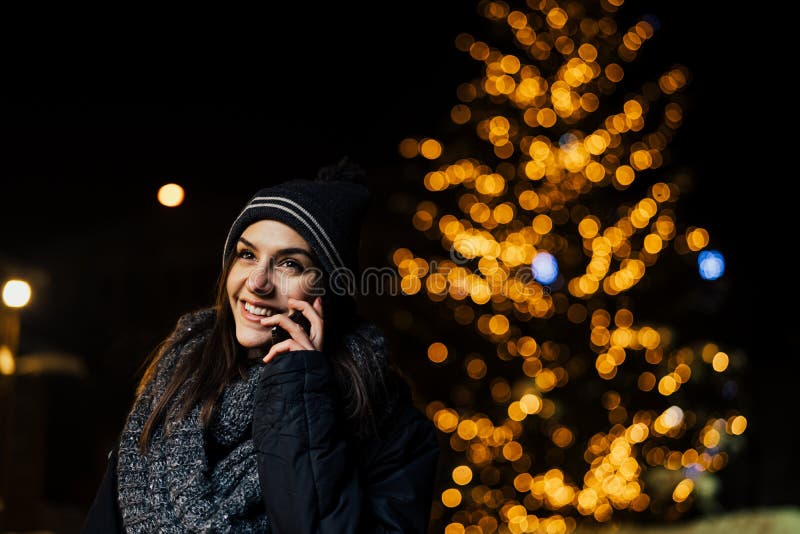 Retrato da noite de uma mulher moreno bonita que usa o smartphone durante o inverno frio no parque Alegria do inverno Feriados de fotografia de stock Retrato da noite de uma mulher moreno bonita que usa o smartphone durante o inverno frio no parque Alegria do inverno Feriados de fotografia de stock