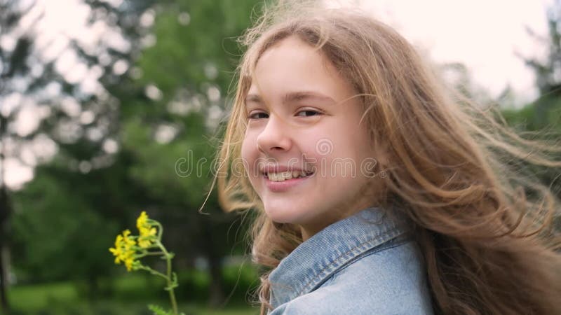 Retrato de adolescente sobre el fondo de árboles verdes. encantadora joven disfrutando de un hermoso día con una flor amarilla en almacen de video