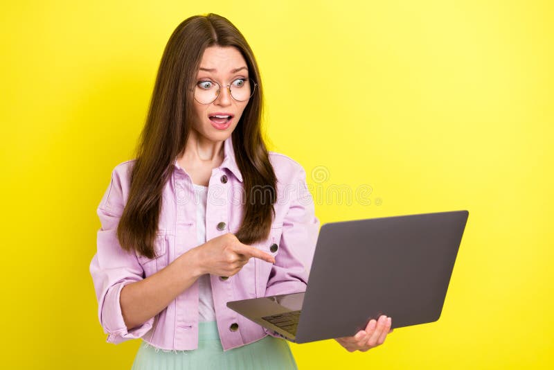 Retrato de atractiva nerviosa y desesperada chica usando un portátil apuntando a la pantalla aislada en color amarillo brillante imagen de archivo