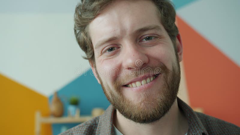 Retrato de clausura de un hombre apuesto y barbudo sonriendo en casa mirando la cámara