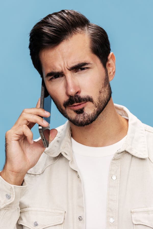 Retrato de cierre de un hombre morena hablando por teléfono disgustado y enojado sobre un fondo azul con una camiseta blanca