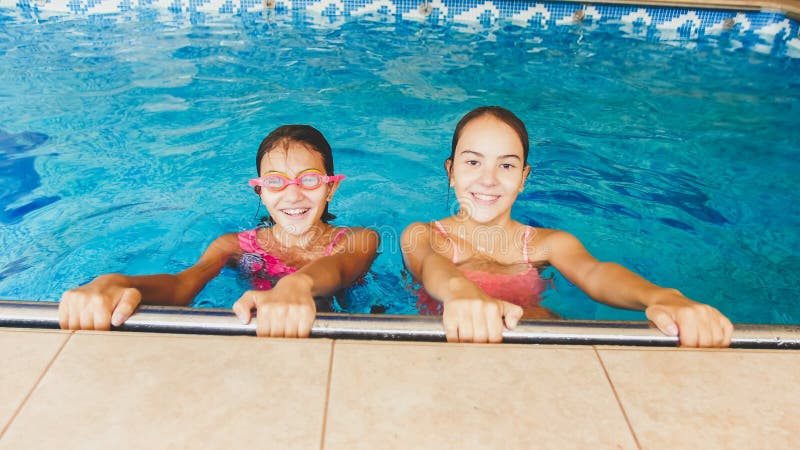 Retrato de dos amigos de muchachas felices que presentan en piscina dentro fotos de archivo libres de regalías Retrato de dos amigos de muchachas felices que presentan en piscina dentro fotos de archivo libres de regalías