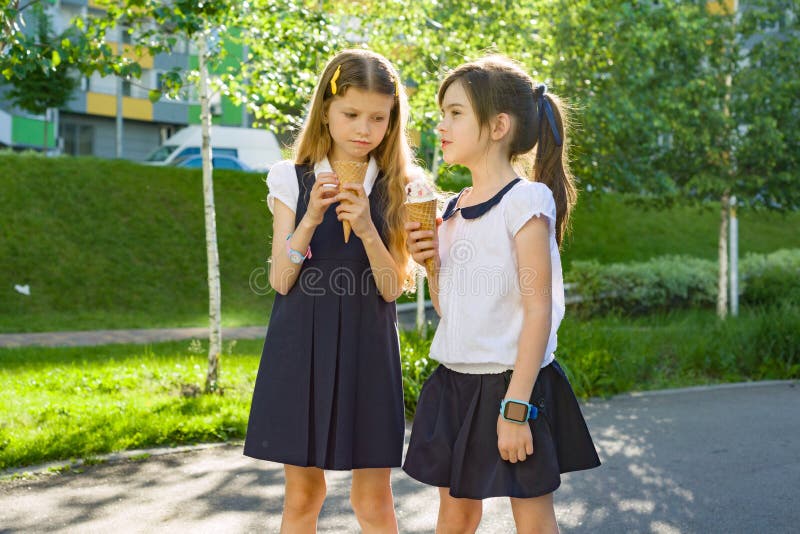 Retrato de duas estudantes das amigas 7 anos velhas na farda da escola que come o gelado
