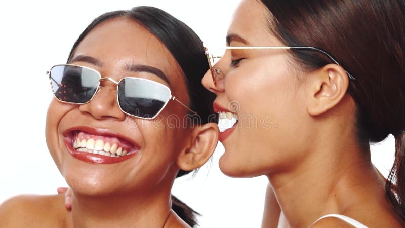 Retrato de duas jovens mulheres asiáticas sorridentes que sorriem a posar em óculos de sol sobre fundo branco