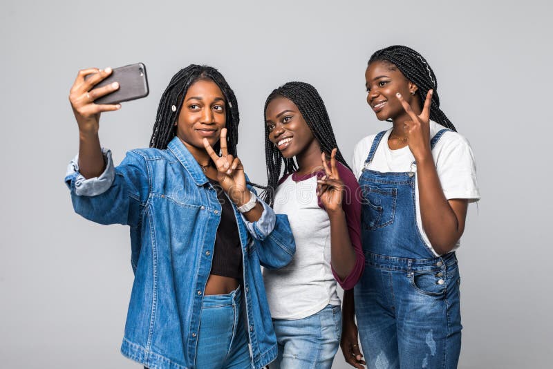 Retrato de encantadoras chicas africanas que disparan selfie en la cámara frontal usando un smartphone gestando un signo de v ais foto de archivo libre de regalías Retrato de encantadoras chicas africanas que disparan selfie en la cámara frontal usando un smartphone gestando un signo de v ais foto de archivo libre de regalías