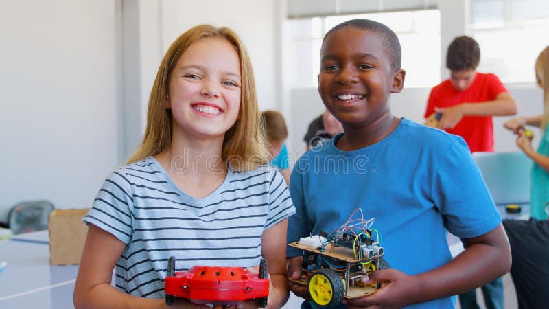 Retrato de estudiantes hombres y mujeres sosteniendo un vehículo robot en clase de codificación de computadoras después de la escuela