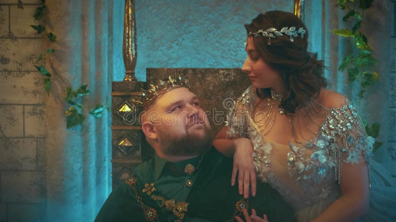 Retrato de fantasía joven reina medieval acariciar marido mirando con amor. la familia real se sienta en el trono metrajes