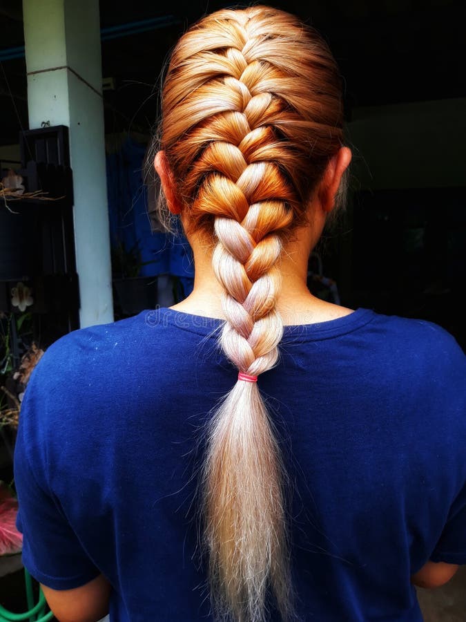 Cabeleireiro secando cabelos loiros à mão com secador de cabelo e escova redonda em um salão de beleza.