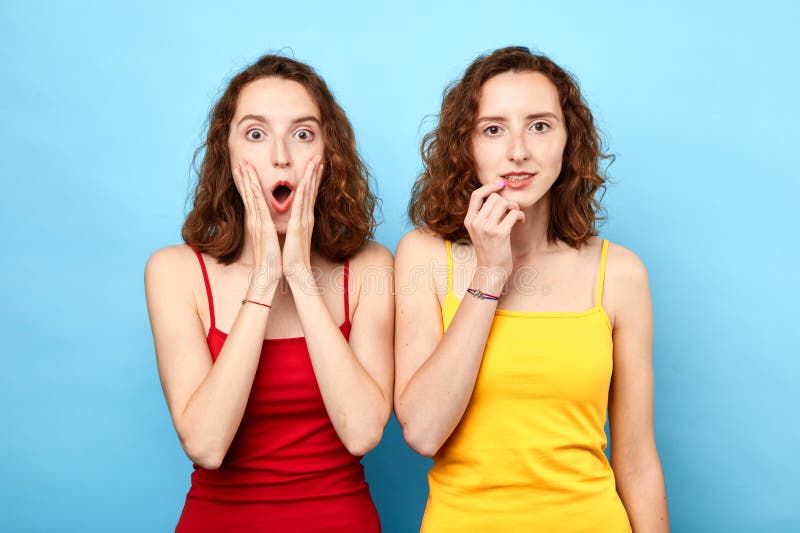 Retrato de hermanas gemelas hermosas en las camisetas rojas y amarillas que muestran emociones fotografía de archivo libre de regalías Retrato de hermanas gemelas hermosas en las camisetas rojas y amarillas que muestran emociones fotografía de archivo libre de regalías