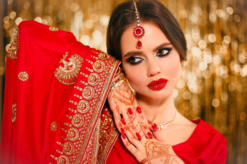 Portrait of beautiful indian girl in red bridal sari over golden bokeh. Young hindu woman model with kundan jewelry. Traditional Indian costume lehenga choli. Henna painting, mehendi on bride`s hands. Portrait of beautiful indian girl in red bridal sari over golden bokeh. Young hindu woman model with kundan jewelry. Traditional Indian costume lehenga choli. Henna painting, mehendi on bride`s hands