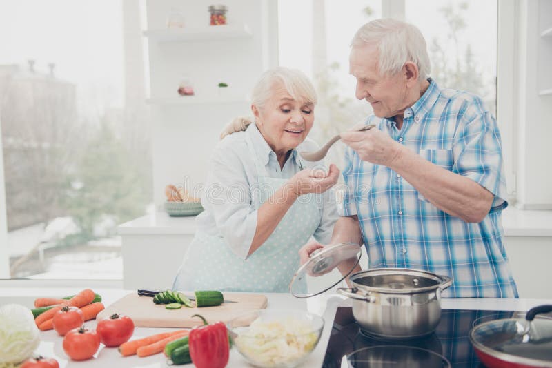 Portrait of lovely nice couple hold hand wooden spoon try soup lunch, table cucumber tomato big room indoors. Portrait of lovely nice couple hold hand wooden spoon try soup lunch, table cucumber tomato big room indoors