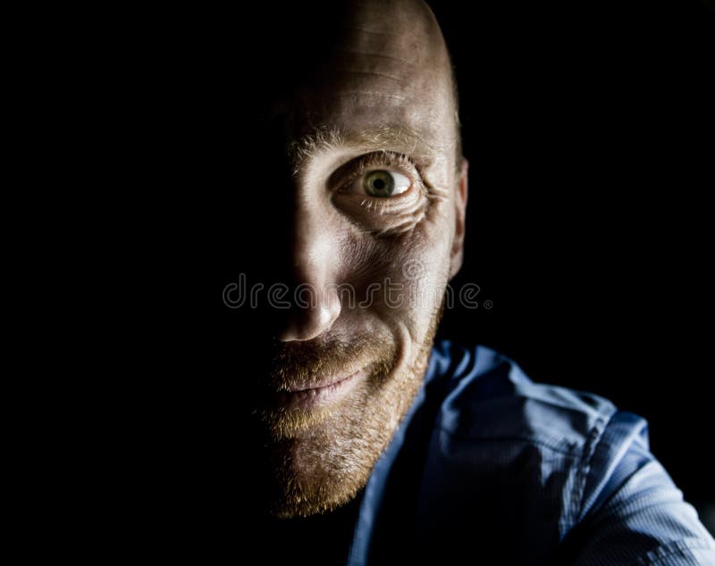 Retrato de hombre caucásico adulto que sonríe como maniático y parece locura. iluminación baja. aislado en negro imagen de archivo libre de regalías