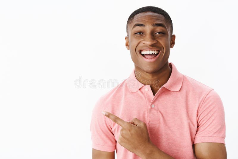 Retrato de impresionado varón joven encantado y sorprendido del afroamericano hermoso carismático en señalar rosado de la camisa fotos de archivo Retrato de impresionado varón joven encantado y sorprendido del afroamericano hermoso carismático en señalar rosado de la camisa fotos de archivo