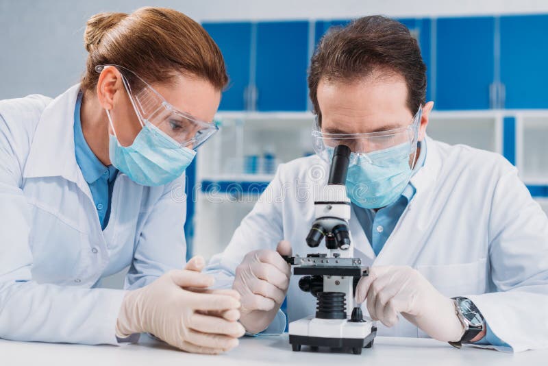 retrato de investigadores en máscaras médicas y de guantes que trabajan con el microscopio junto foto de archivo retrato de investigadores en máscaras médicas y de guantes que trabajan con el microscopio junto foto de archivo