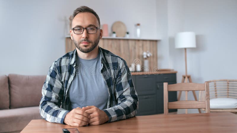 Retrato de joven barbudo en gafas de moda relajándose sentados en la mesa en la sala de estar de casa