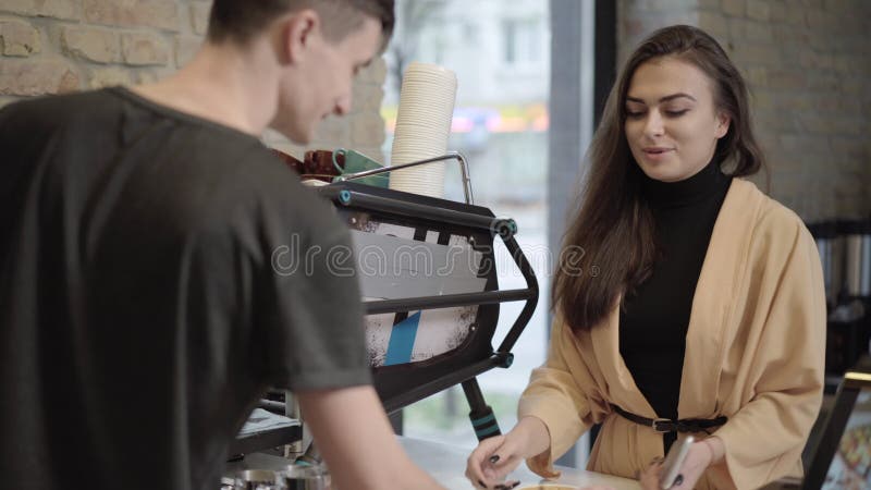 Retrato de joven hermosa mujer comprando café. barista masculino sirviendo a una hermosa morena caucásica señora en el café