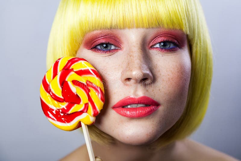 Retrato de la belleza del modelo femenino joven lindo con las pecas, maquillaje rojo y peluca amarilla, sosteniendo el palillo co fotos de archivo libres de regalías Retrato de la belleza del modelo femenino joven lindo con las pecas, maquillaje rojo y peluca amarilla, sosteniendo el palillo co fotos de archivo libres de regalías
