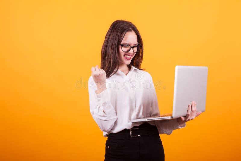 Retrato de la chica joven feliz que mira y que se sostiene el ordenador portátil del ther sobre fondo amarillo imagen de archivo Retrato de la chica joven feliz que mira y que se sostiene el ordenador portátil del ther sobre fondo amarillo imagen de archivo