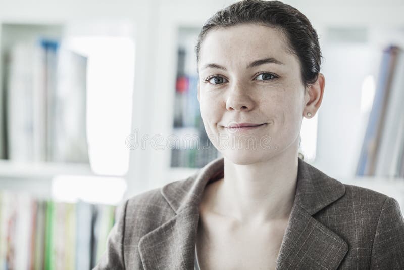 Retrato de la empresaria joven sonriente que mira la cámara, el principal y los hombros imagen de archivo Retrato de la empresaria joven sonriente que mira la cámara, el principal y los hombros imagen de archivo