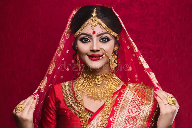 Retrato de la joyer?a del oro de la novia que lleva india joven y de la sari roja en la boda fotografía de archivo libre de regalías Retrato de la joyer?a del oro de la novia que lleva india joven y de la sari roja en la boda fotografía de archivo libre de regalías