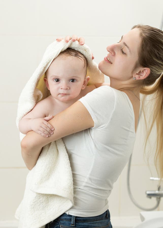 Retrato de la madre joven que limpia a su bebé con la toalla grande después que tiene ducha fotografía de archivo Retrato de la madre joven que limpia a su bebé con la toalla grande después que tiene ducha fotografía de archivo