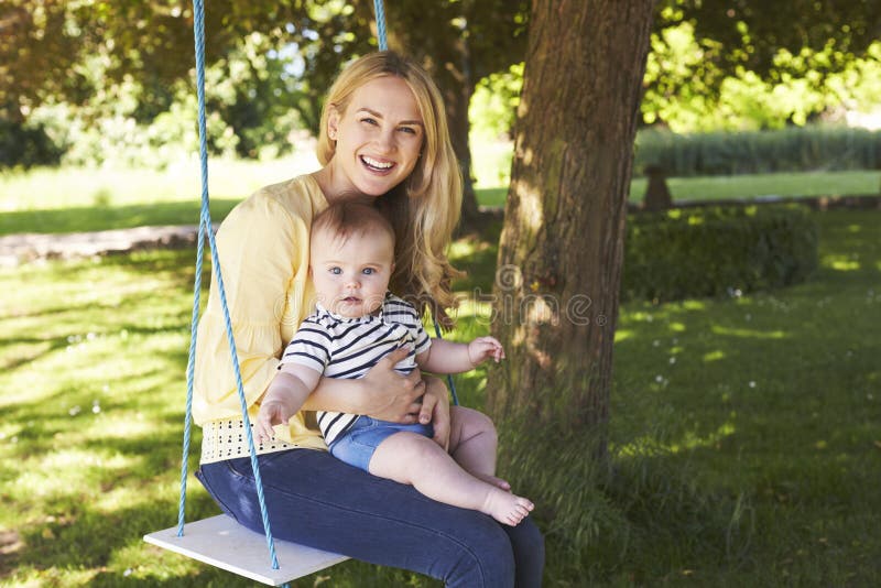 Retrato de la madre que juega con el hijo del bebé en el oscilación del jardín imagenes de archivo Retrato de la madre que juega con el hijo del bebé en el oscilación del jardín imagenes de archivo