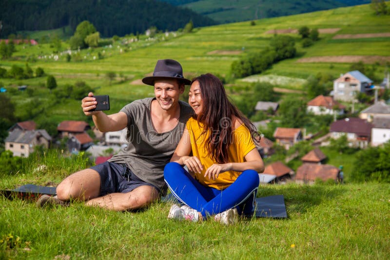 Retrato de la muchacha alegre y del muchacho que se sientan en la montaña y que hacen el selfie imagenes de archivo Retrato de la muchacha alegre y del muchacho que se sientan en la montaña y que hacen el selfie imagenes de archivo