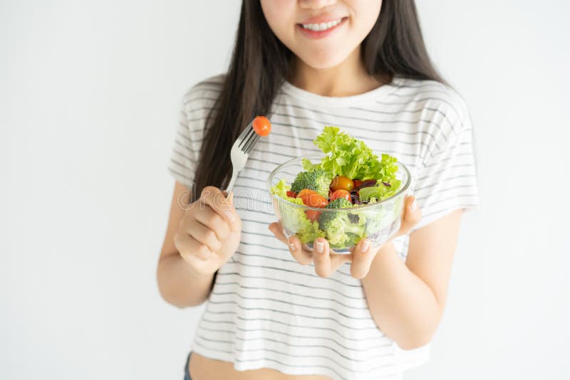 Retrato de la mujer asiática que sonríe y que come la ensalada en el fondo blanco en casa, la comida para la atención sanitaria y foto de archivo Retrato de la mujer asiática que sonríe y que come la ensalada en el fondo blanco en casa, la comida para la atención sanitaria y foto de archivo
